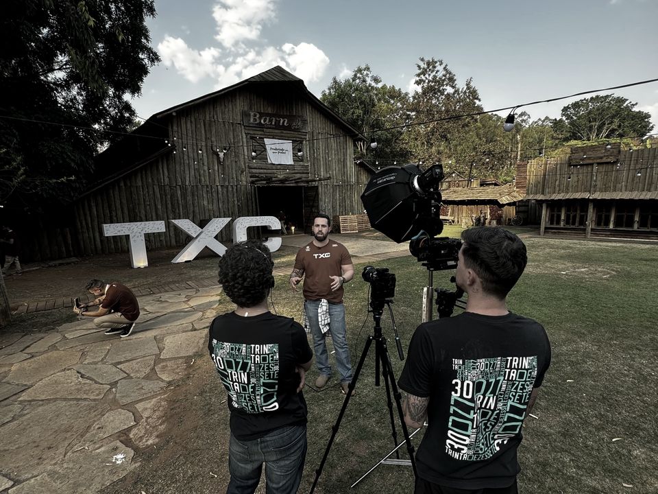 Caiube em gravação externa da TXC, com equipe e câmeras em frente a um galpão