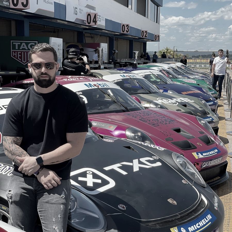 Caiube ao lado de carros de corrida com a marca TXC no autódromo